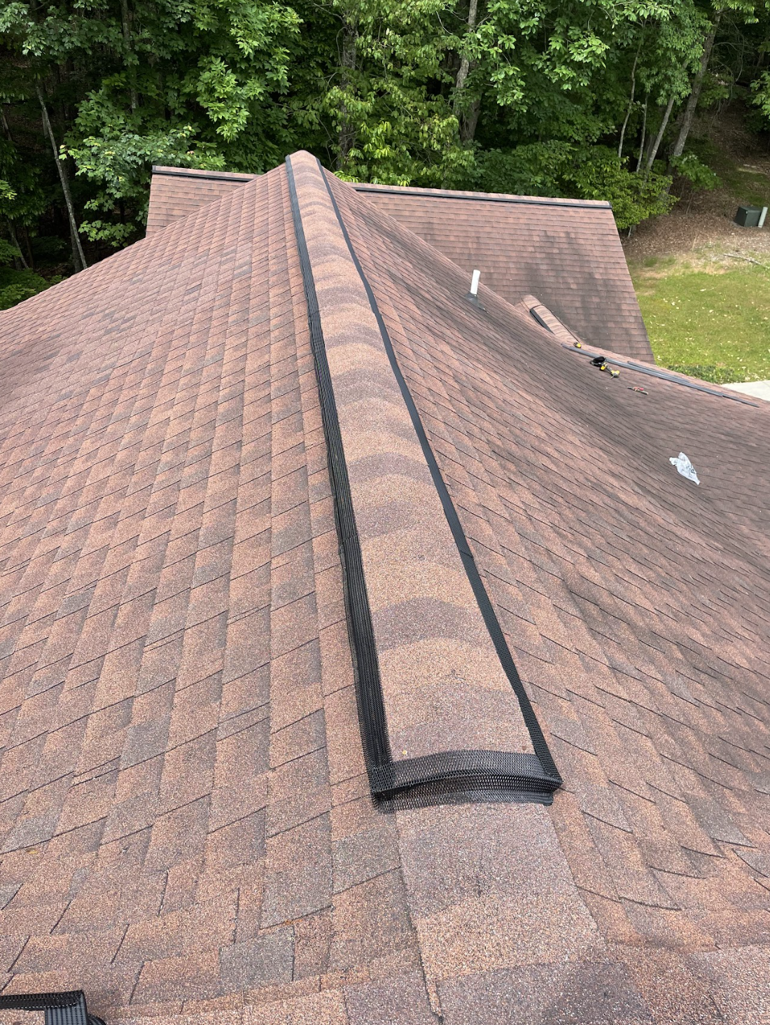 Metal ridge vent installed on a residential roof replacing degraded builder-grade vent